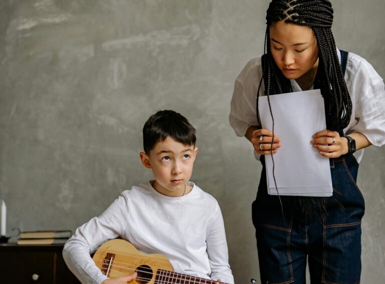 Boy learning ukulele with music teacher guidance, indoors setting.